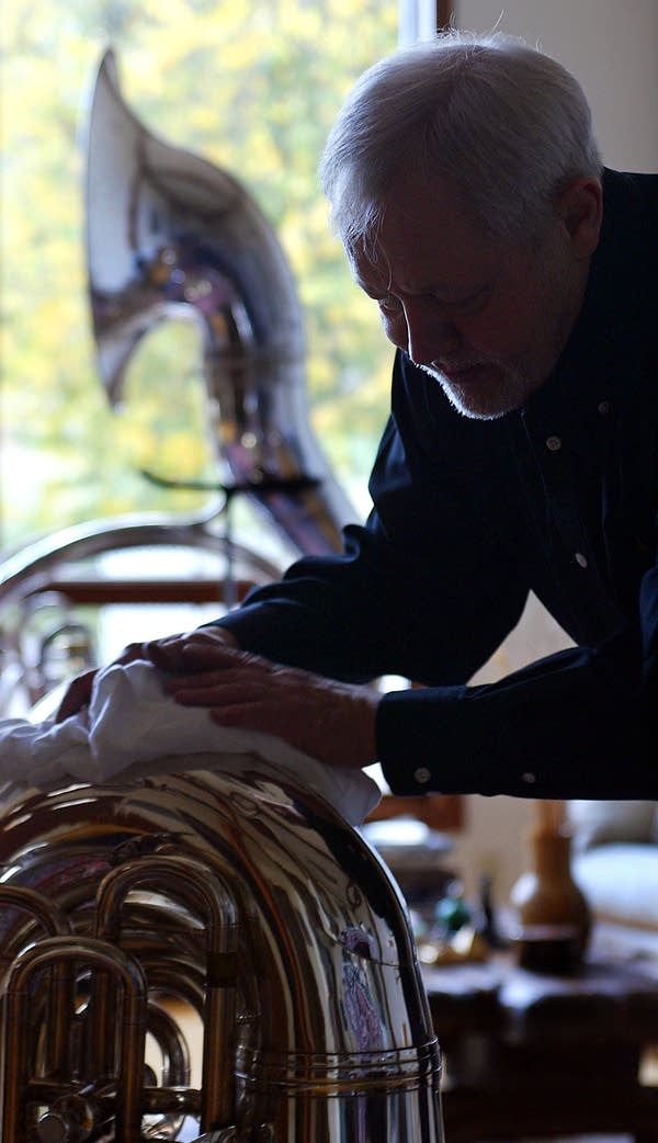 A man polishes a tuba in a home studio