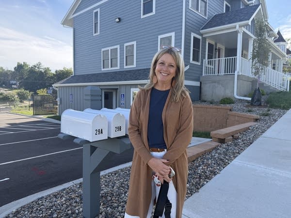 A woman stands next to mailboxes in front of a light blue house.