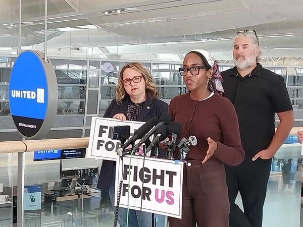 A woman speaks at a podium with a man and woman by her side. The podium has a sign that reads, "Fight for us."