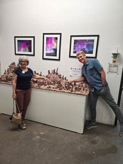 A man and a woman pose next to a sculpture in a gallery.