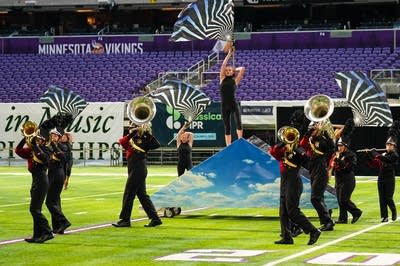 A marching band performs on the field of a football stadium.