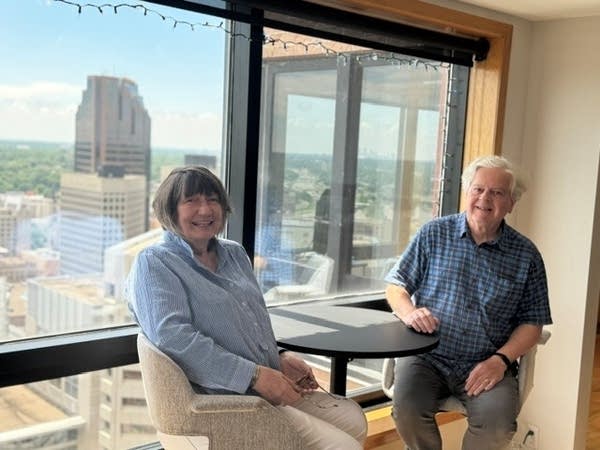 Two people sit at a table with a city view though the window.