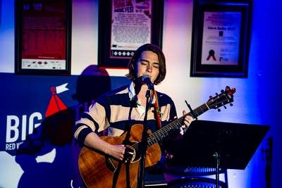 A musician sings and plays guitar onstage in a small venue