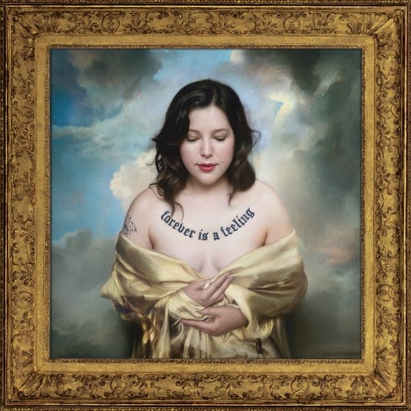 Framed portrait of a woman in a gown with the words 'Forever is a Feeling' tattooed on her chest in Gothic typeface