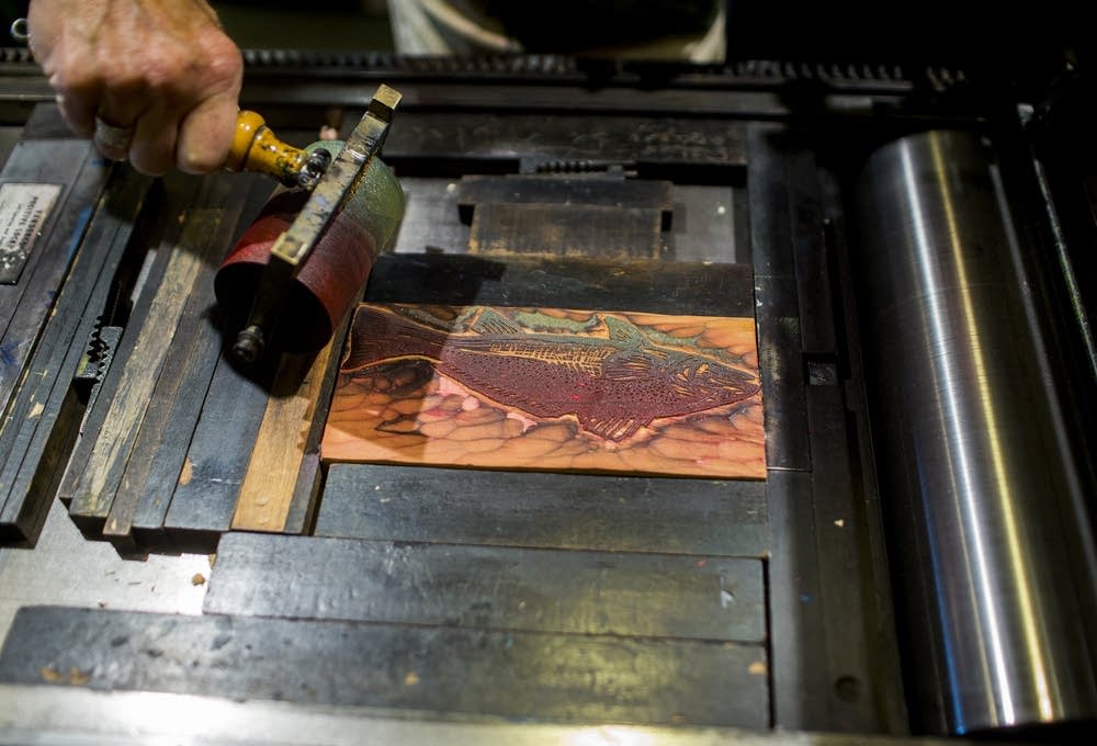 Bowen applies ink to a red fish wood block.