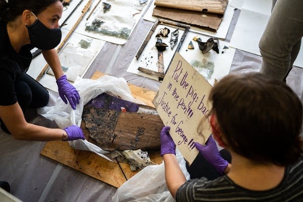 Two people sort burnt art on the floor.