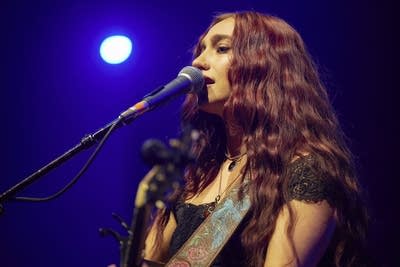 A woman sings and plays guitar onstage in a large music venue