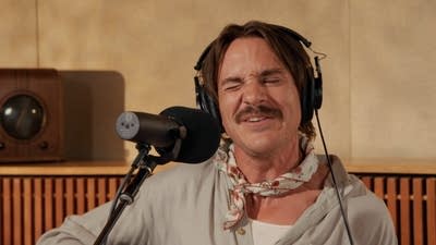 A musician sings and plays guitar in a recording studio