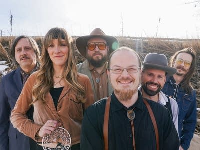 Six people stand among frozen cattails and snow during early Minnesota spring
