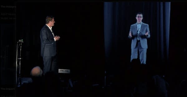 Man standing on stage with hologram of another man