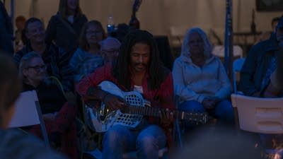 a crowd of people playing music around a campfire 