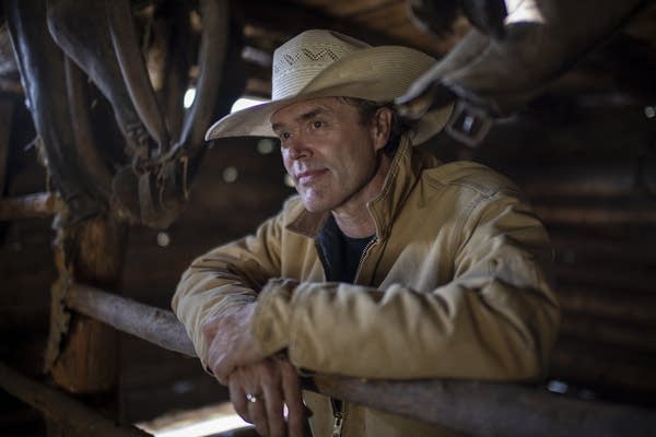 A man in a cowboy hat leans on a railing in a barn