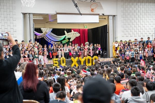 A large celebration is held in a crowded multipurpose room with a stage.