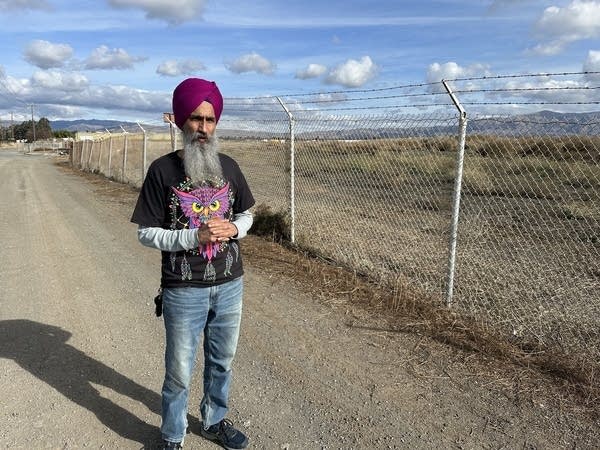 Taran Singh, a man wit ha beard, turban, t-shirt, long-sleeve shirt and jeans, stands near undeveloped land.