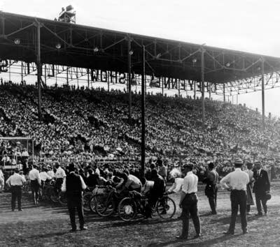 A black and white photo of the Grandstand full of people watch a motorcycle race