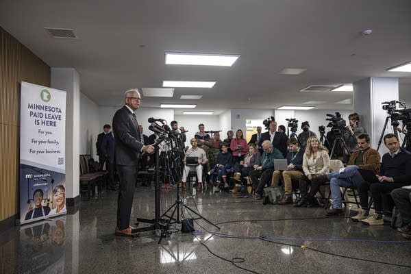 Gov. Tim Walz speaks at a podium, with a number of people standing behind him.