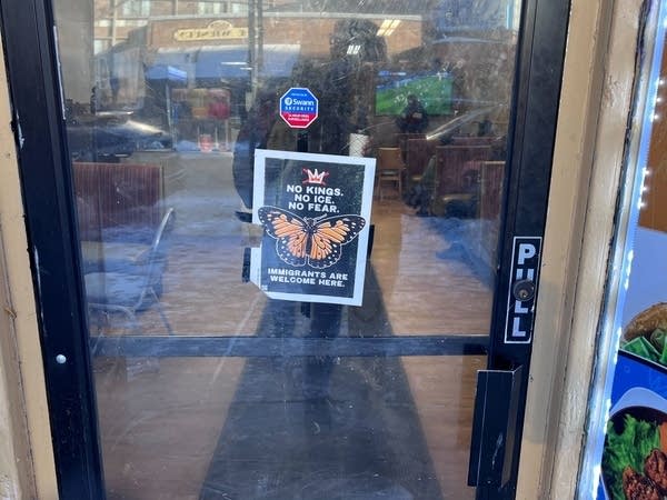 A sign hanging on a glass door with a monarch butterfly that reads, "NO KINGS. NO ICE. NO FEAR. IMMIGRANTS ARE WELCOME HERE."