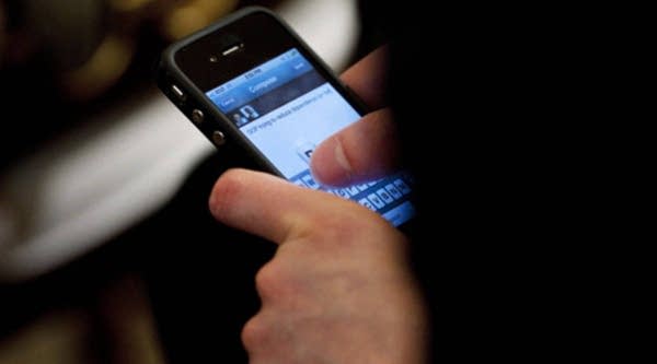 An audience member uses an iPhone to send a tweet during an online Twitter town hall meeting with U.S. President Barack Obama from the East Room of the White House July 6, 2011 in Washington, D.C.