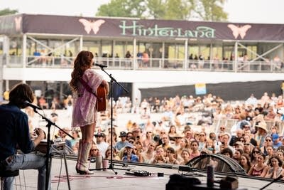 Two musicians performing on a large outdoor stage before large audience