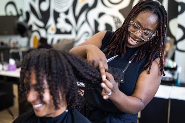 A Black woman styles a woman's hair