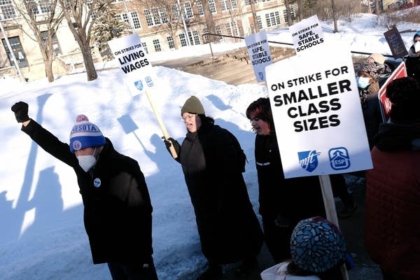 People hold signs and walk along the sidewalk.