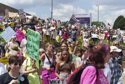 People hold signs and yell during a rally outside.