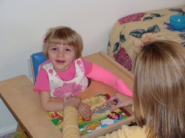 A toddler dressed in pink with a matching cast plays with a puzzle.