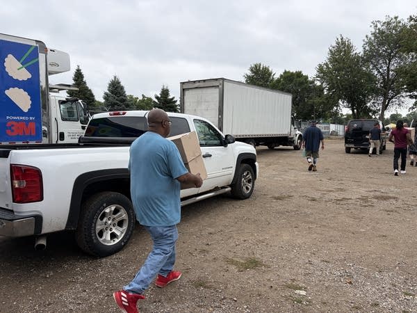 A man carries cardboard boxes behind a pickup truck.