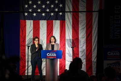 Wide shot of Angie Craig giving a concession speech in front of a large American flag.