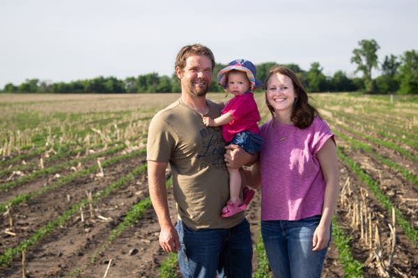 A man holding a child and woman standing in a field