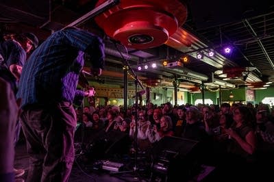 Crowd watching performance inside Turf Club with light from windows coming in.