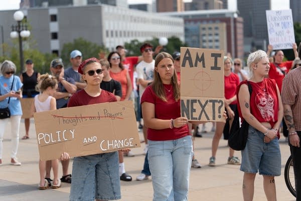 Teenagers stand at a protest holding cardboard signs.