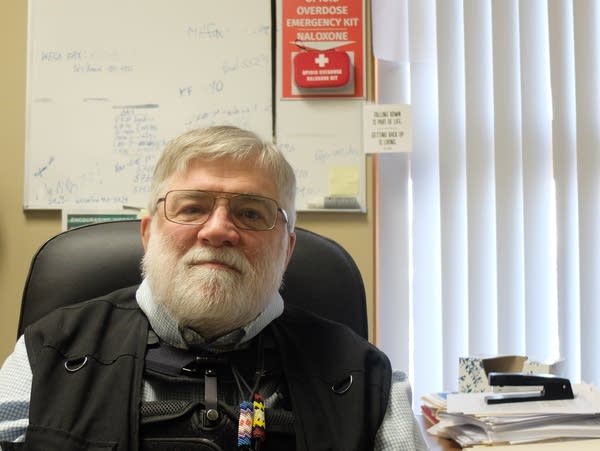 A man sits in his office chair next to a somewhat cluttered desk