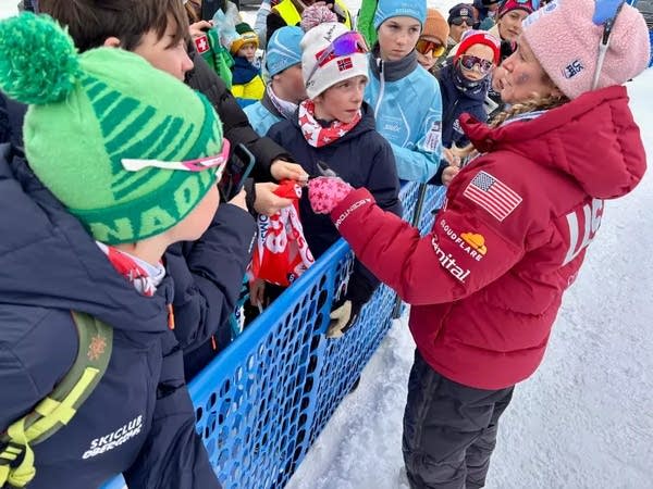 Jessie Diggins stands next to a crowd of fans standing behind a blue plastic fence.