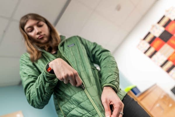 A young woman with cerebral palsy zips up a green jacket.
