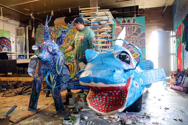 A man stands next to bright blue, purple and red artworks of a four-legged animal and a fish.