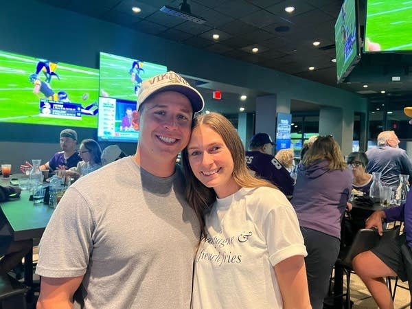 A man and woman pose for a photo together at a busy sportsbar.