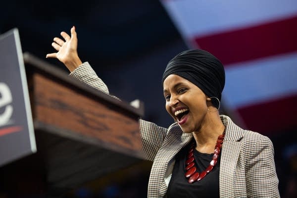 A woman smiles and waves as she walks to a podium.