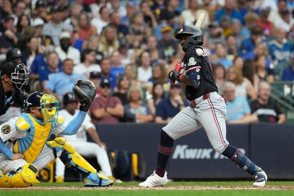 A Twins baseball player turns his back as a pitch hits him at the plate.