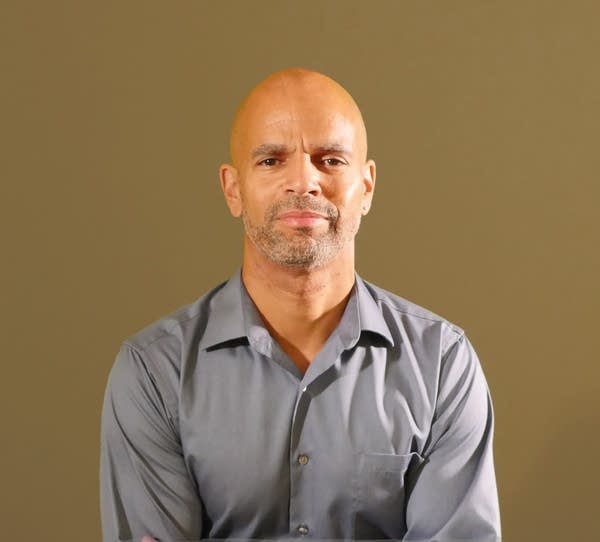 A man in a gray collared shirt smiles at the camera. 