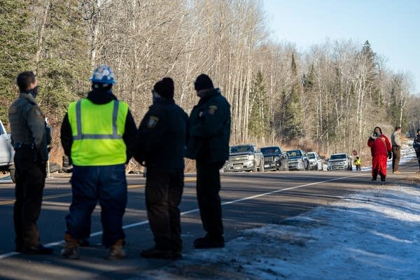 People stand in a road as a woman in red yells at them from a distance.