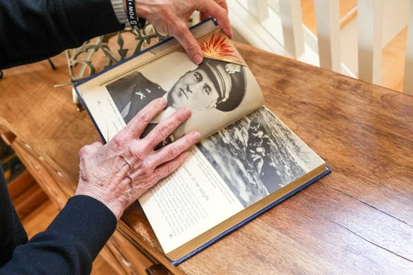 Two hands hold open a book with a photograph of a soldier printed inside.