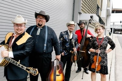 Five people standing outdoors holding string instruments