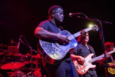 A musician sings and plays guitar onstage in a large music venue