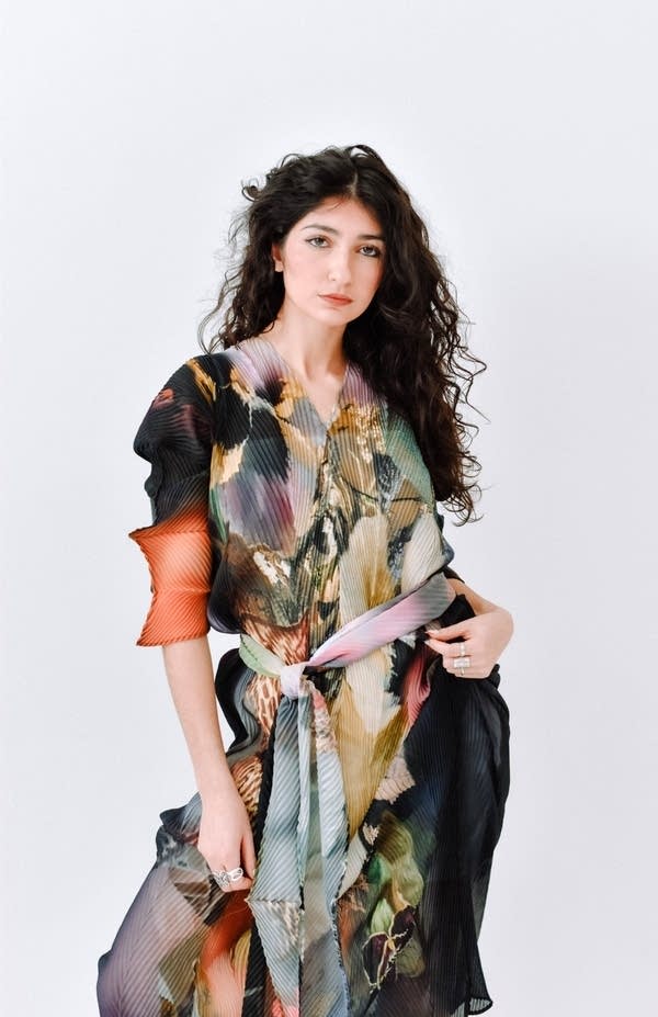 Portrait of a woman standing in front of a white wall, wearing a floral dress.