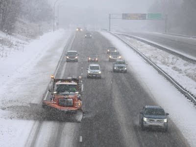 A snowplow clears an interstate in front of several cars.