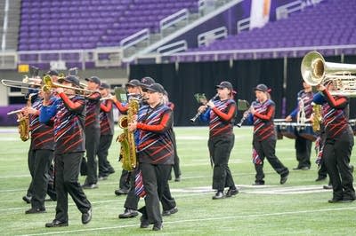 A marching band performs on the field of a football stadium.
