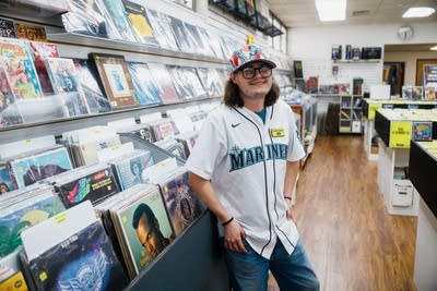 A person stands next to a large display of vinyl records in a record store