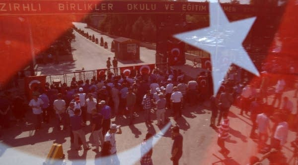 People are seen through a Turkish flag as they block the entrance of the Armored troops school in the capital of Ankara.