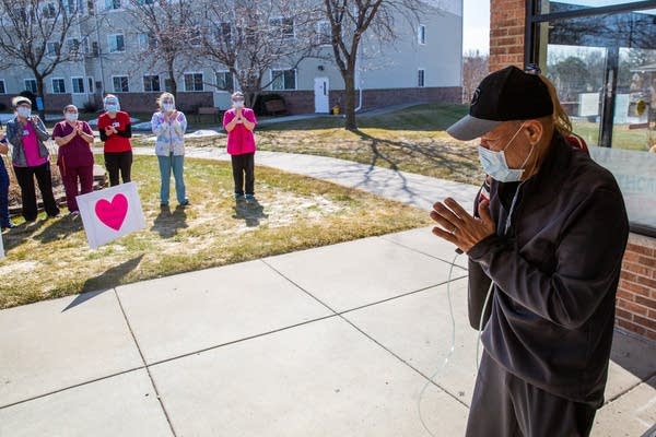 A man waves to a line of nurses while walking out of a building.